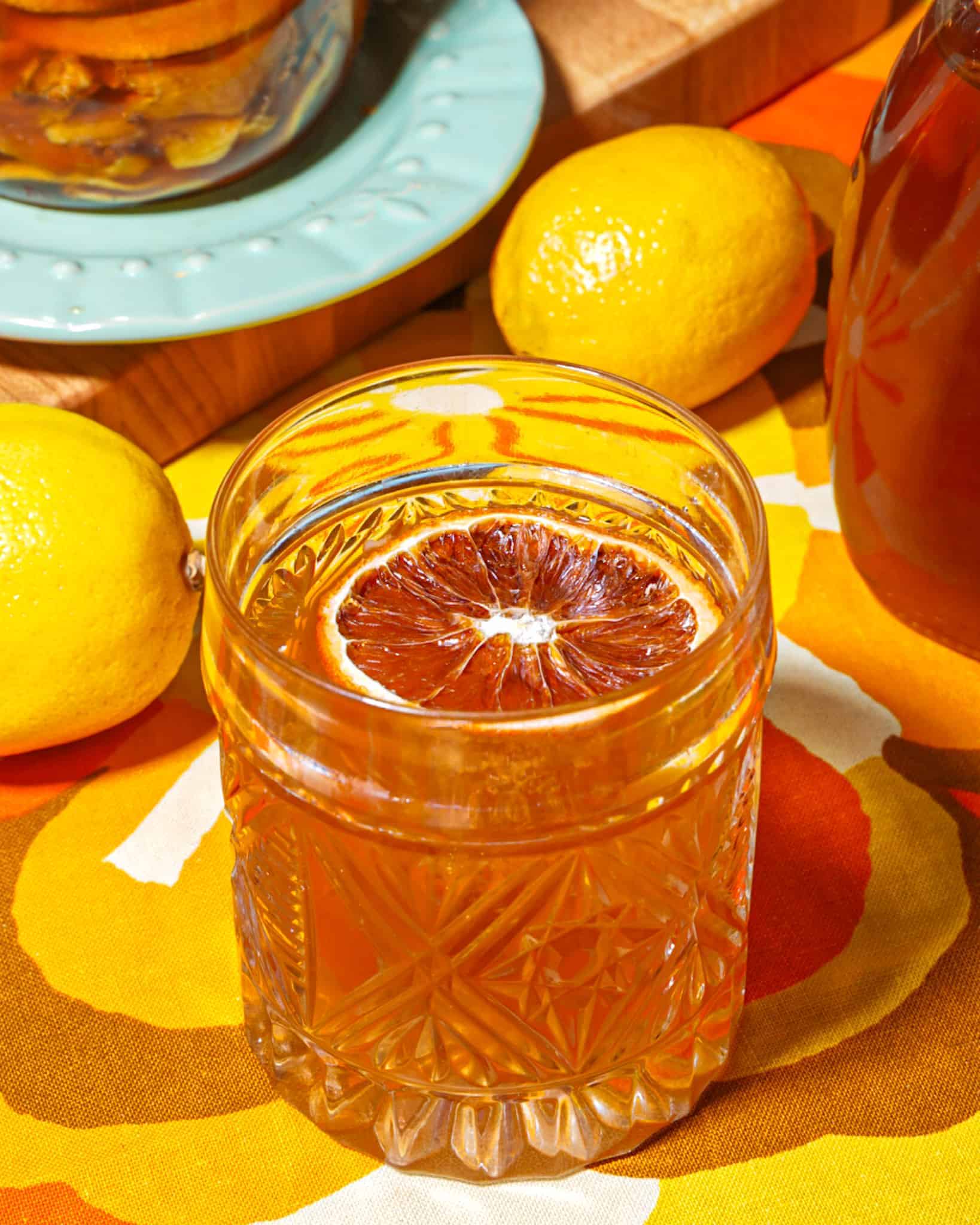 Glass of brown liquid (honey old fashion cocktail), garnished with dehydrated orange slice lemons, h