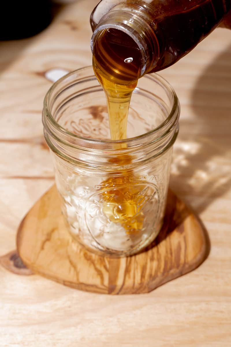 person pouring honey into mason jar of peeled garlic cloves