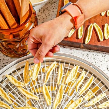 drying pasta on dehydrator trays with person placing pasta in tray
