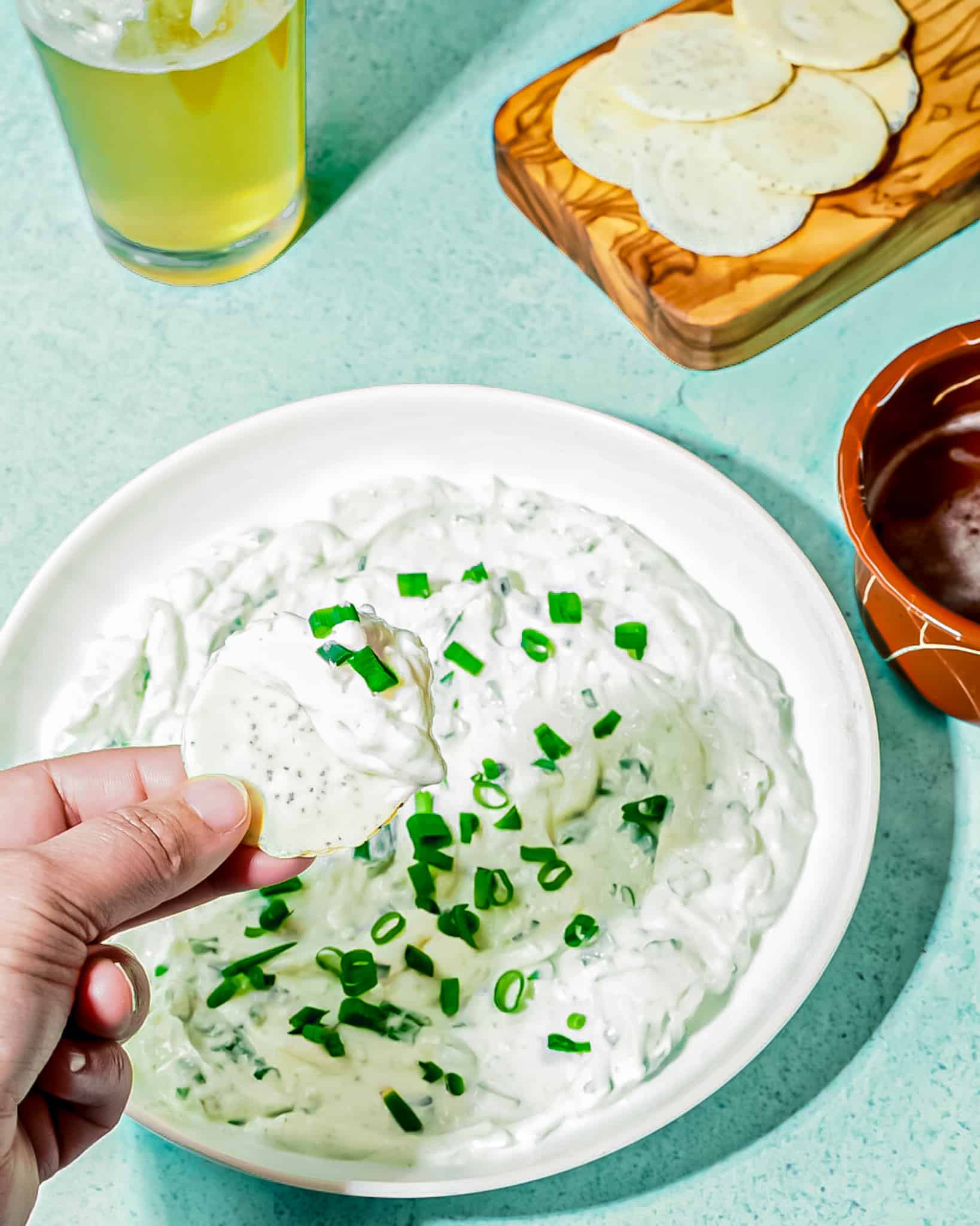 Person holding round cracker with sour cream onion dip topped with scallions