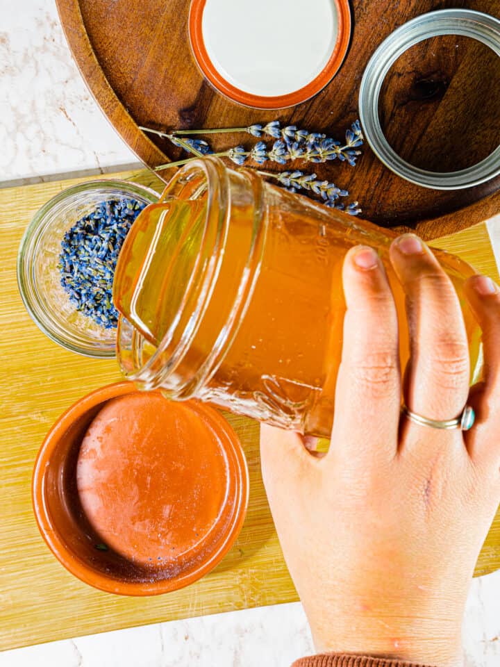 person pouring raw honey on to dried lavender flowers in a mason jar