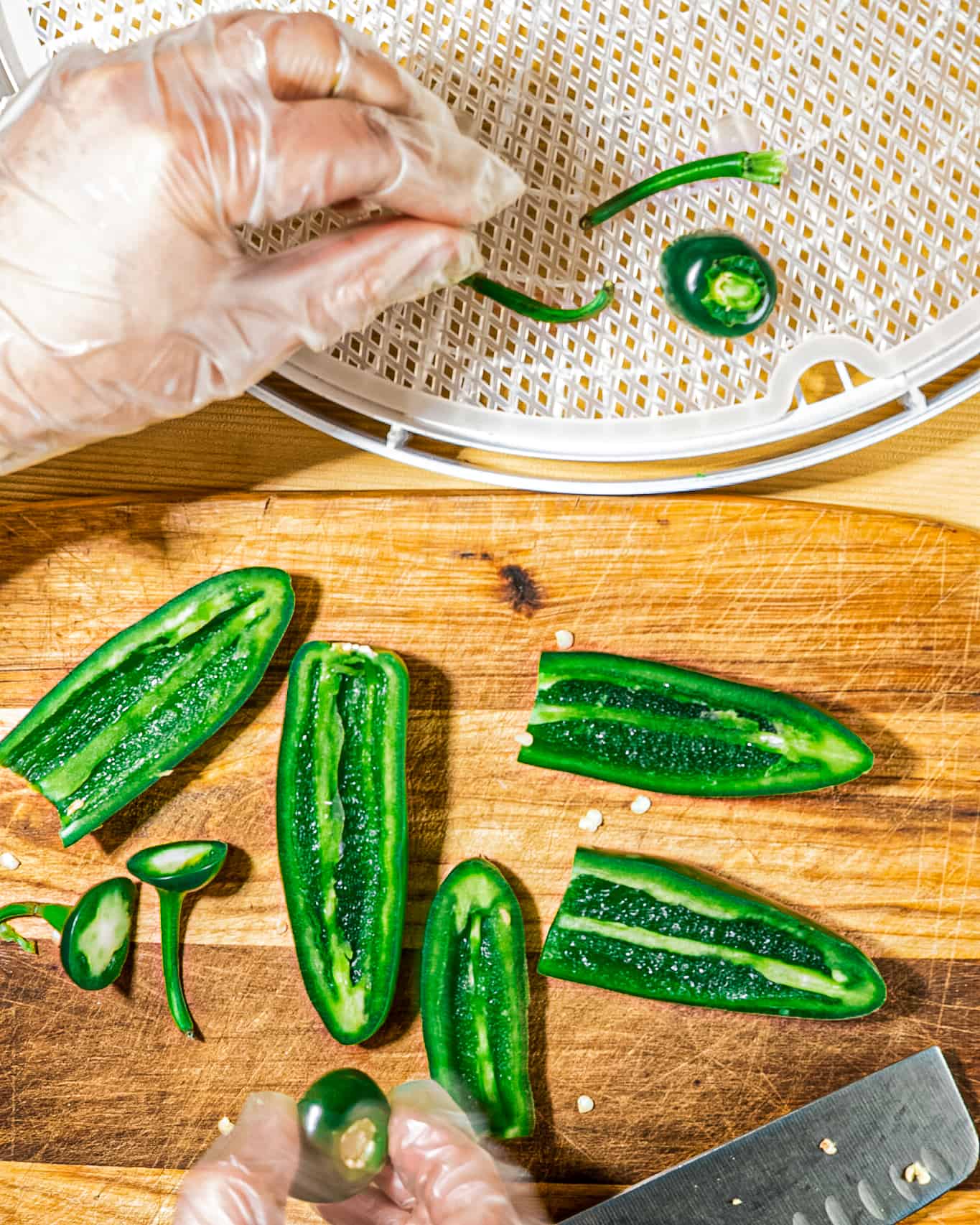 jalapeno peppers on a wooden cutting board and person placing pieces on dehydrator tray