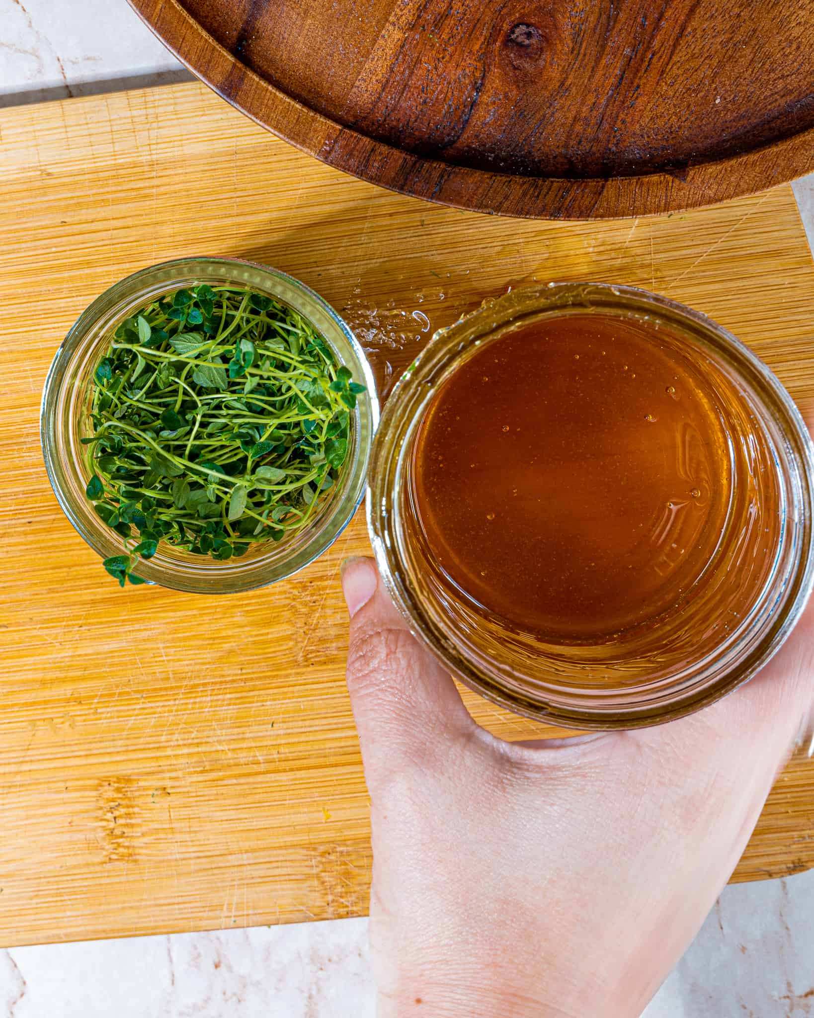 person with jar of honey next to small jar full of sprigs of thyme