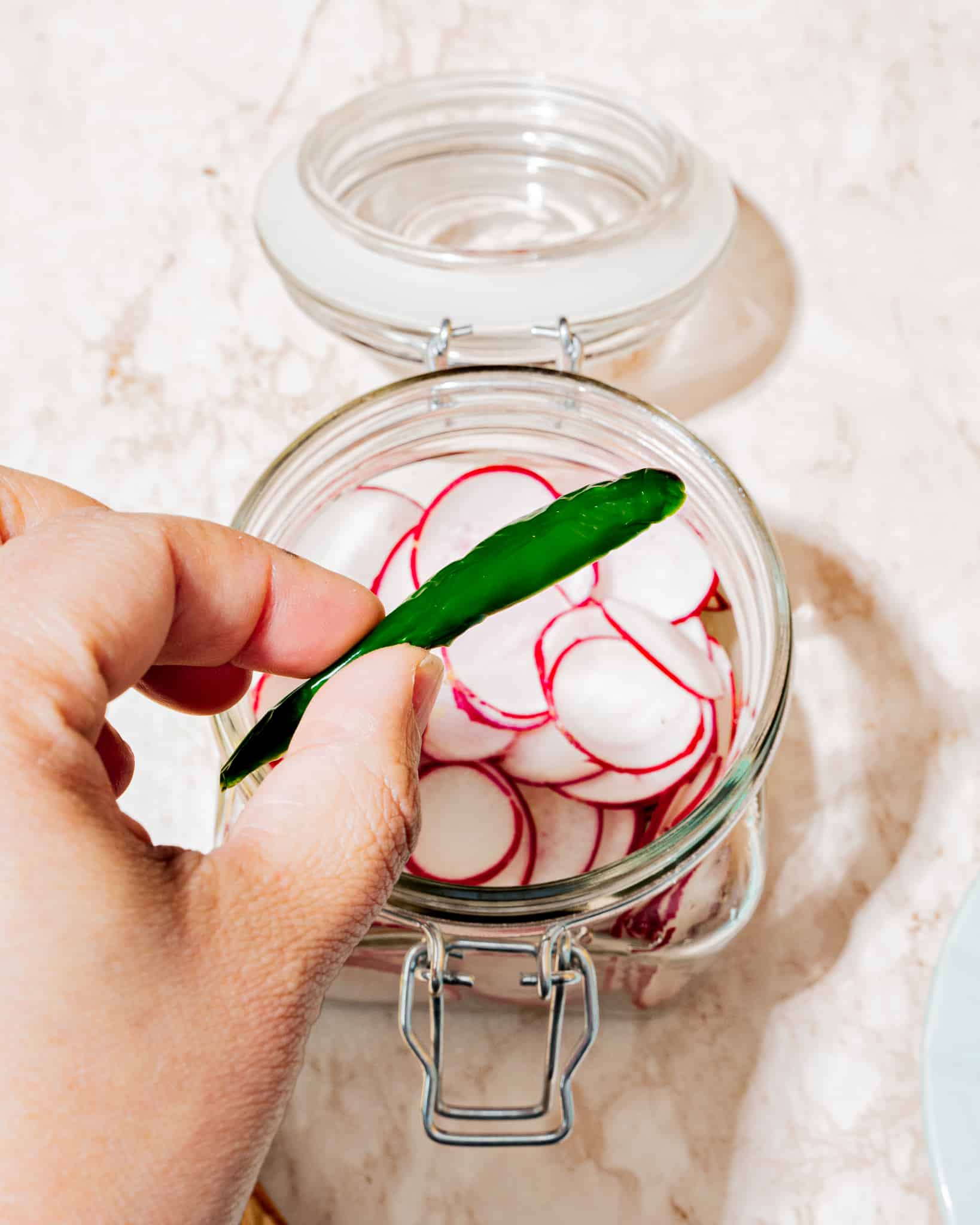 Person adding pepper to glass jar full of radishes