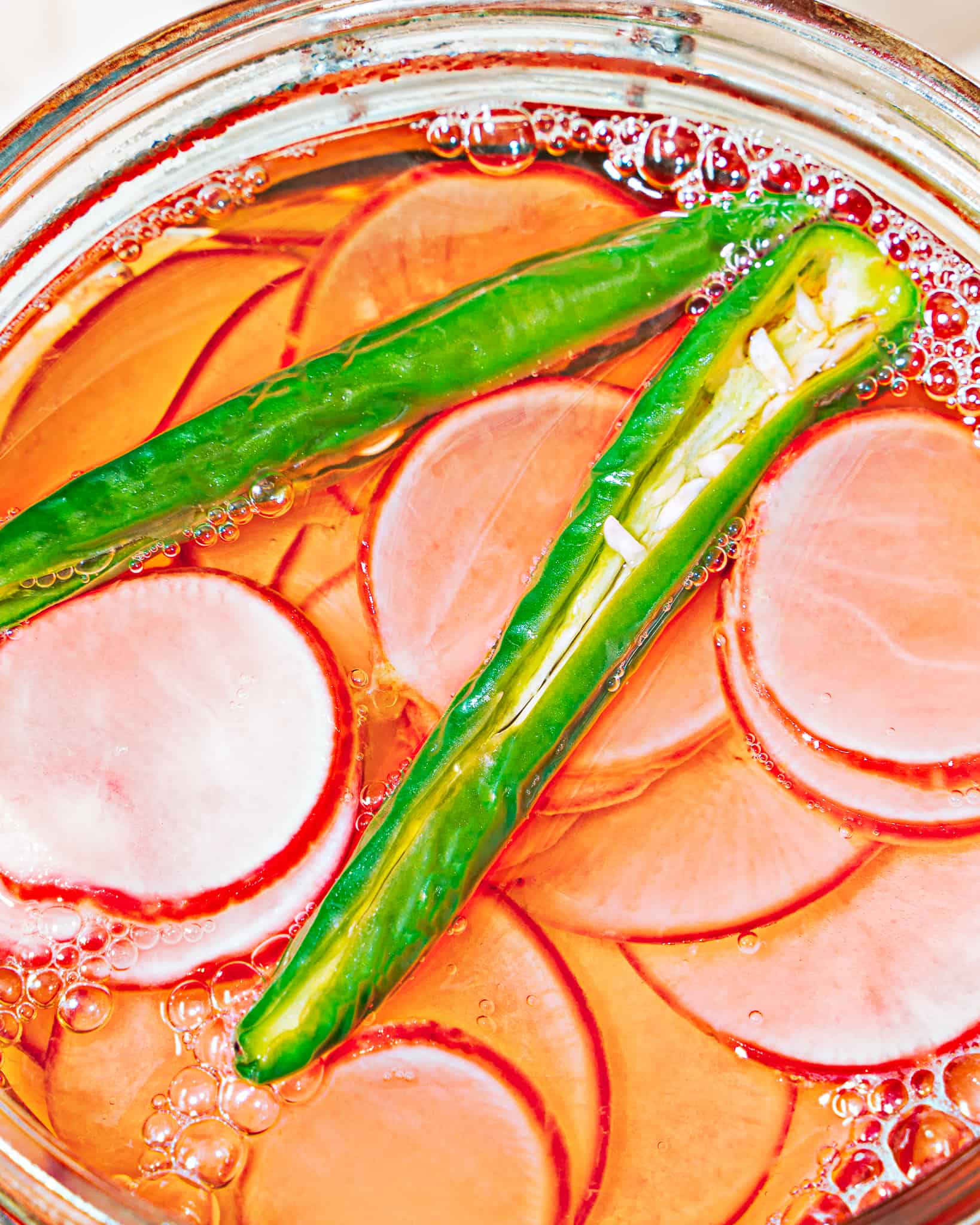 close up of glass jar with radish slices and sliced serrano peppers