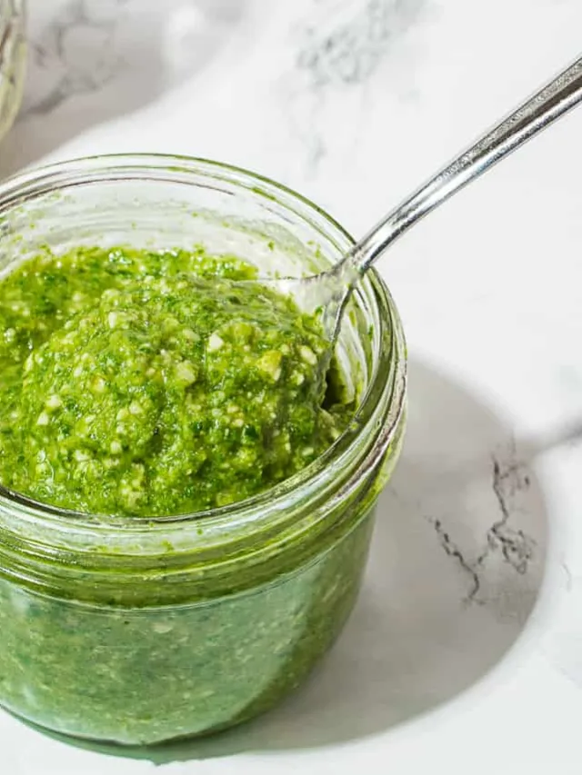 glass jar with green pasta pesto sauce on a white marble background