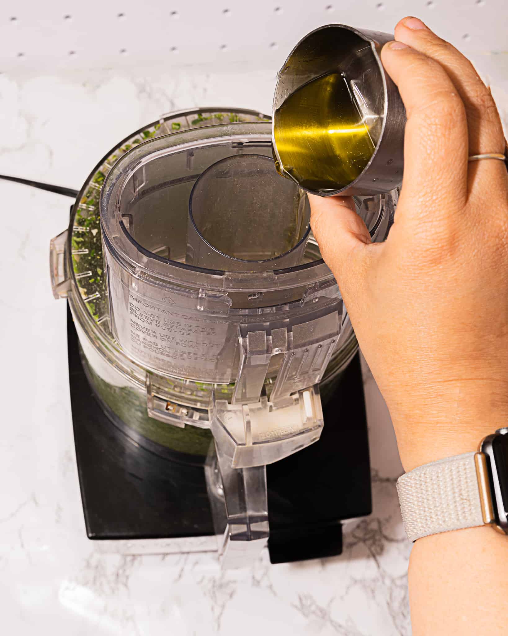 person adding olive oil to top of food processor