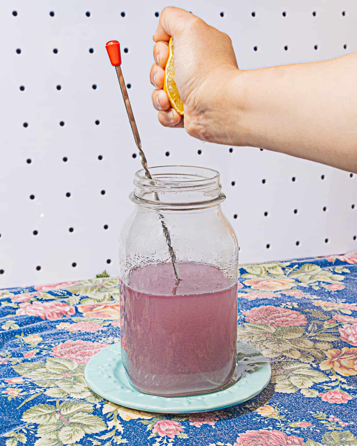 person squeezing lemon into mason jar filled with light purple liquid