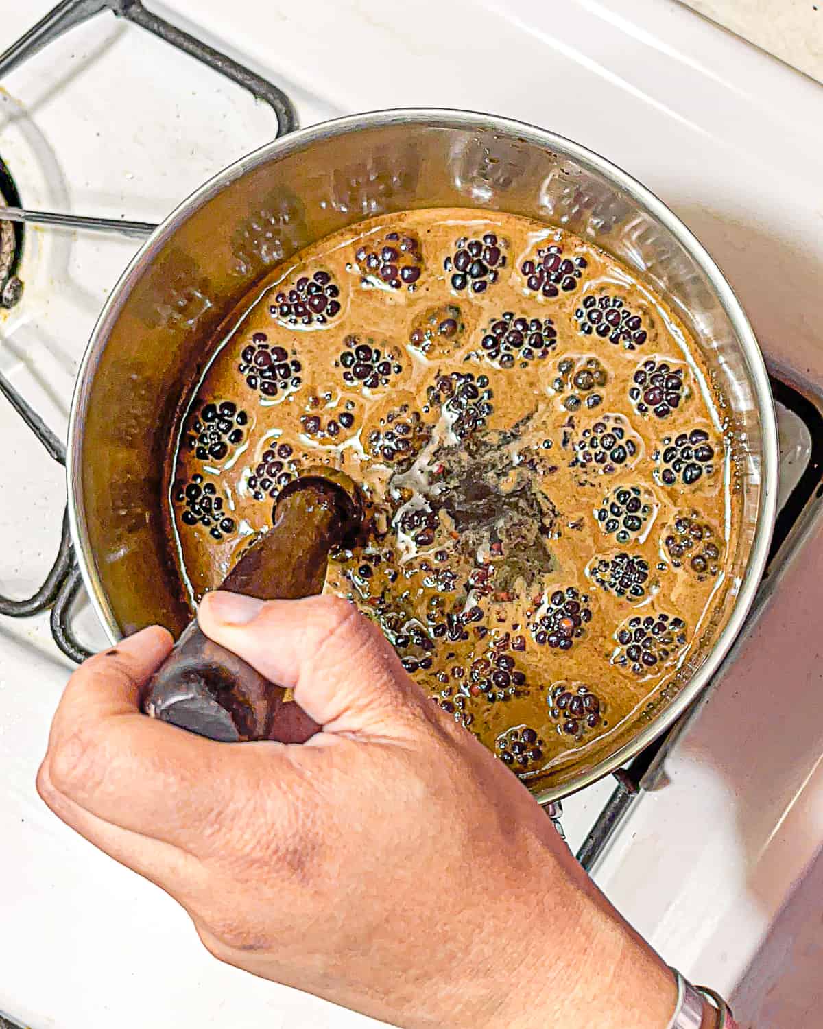 person muddling blackberries in sugar water over stove