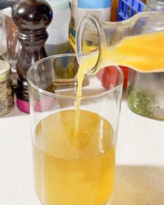 person pouring peach nectar into peach green tea lemonade into a tall glass mizer