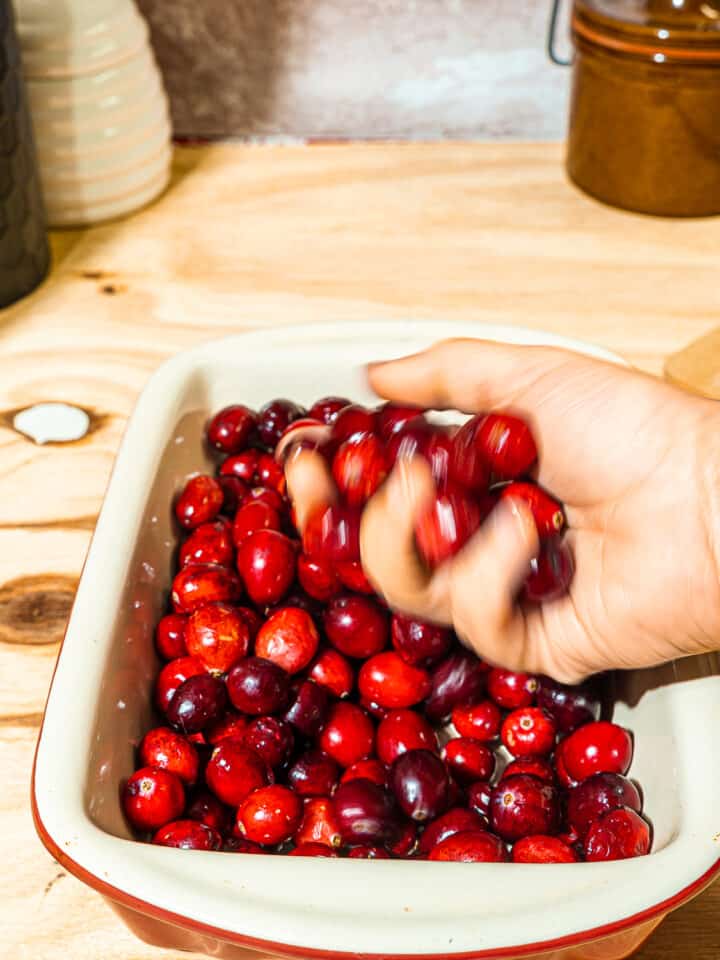 person holding cranberries over a small baking dish