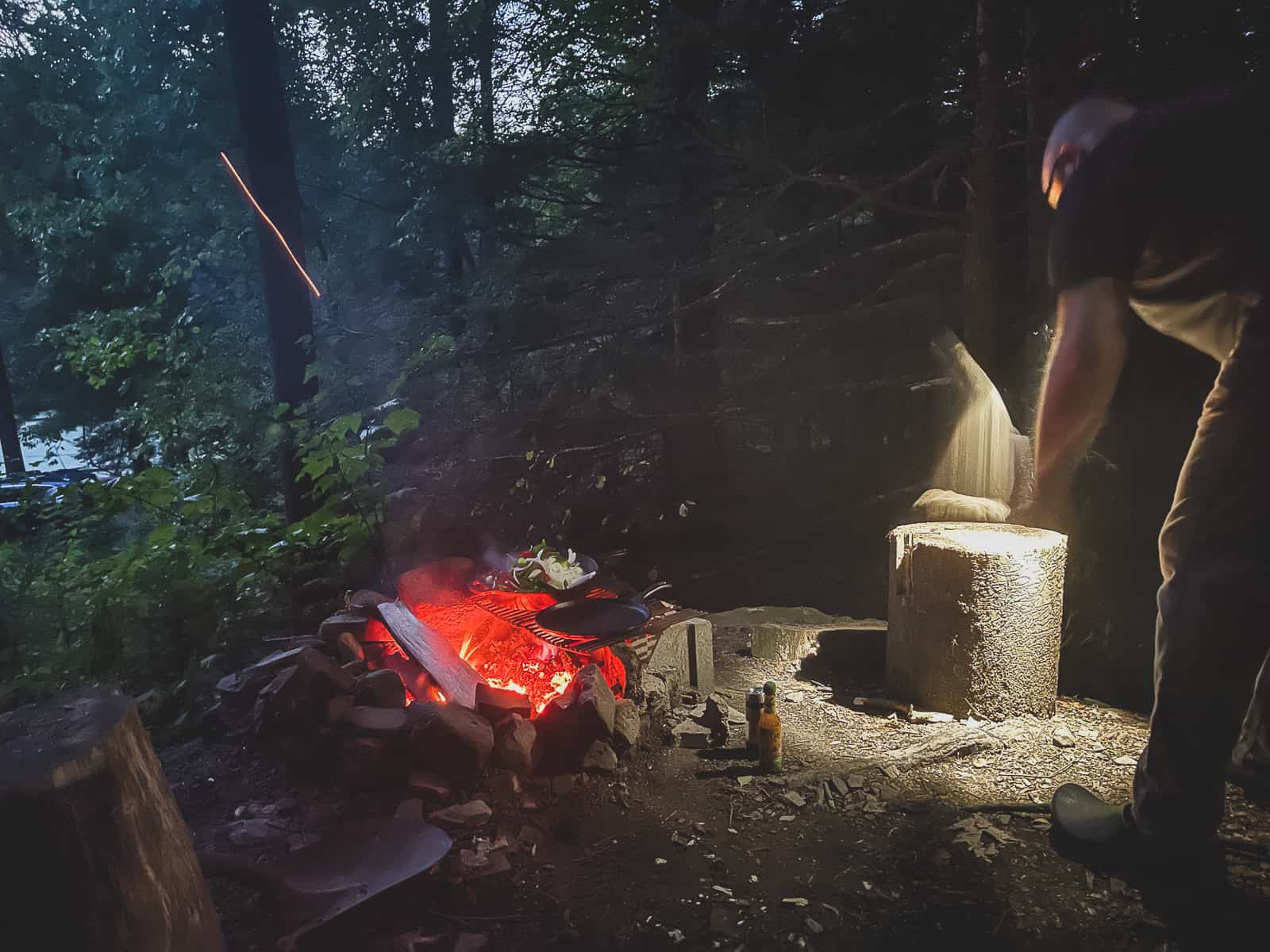 person shining light over open fire with cooking grate and cast iron skillet