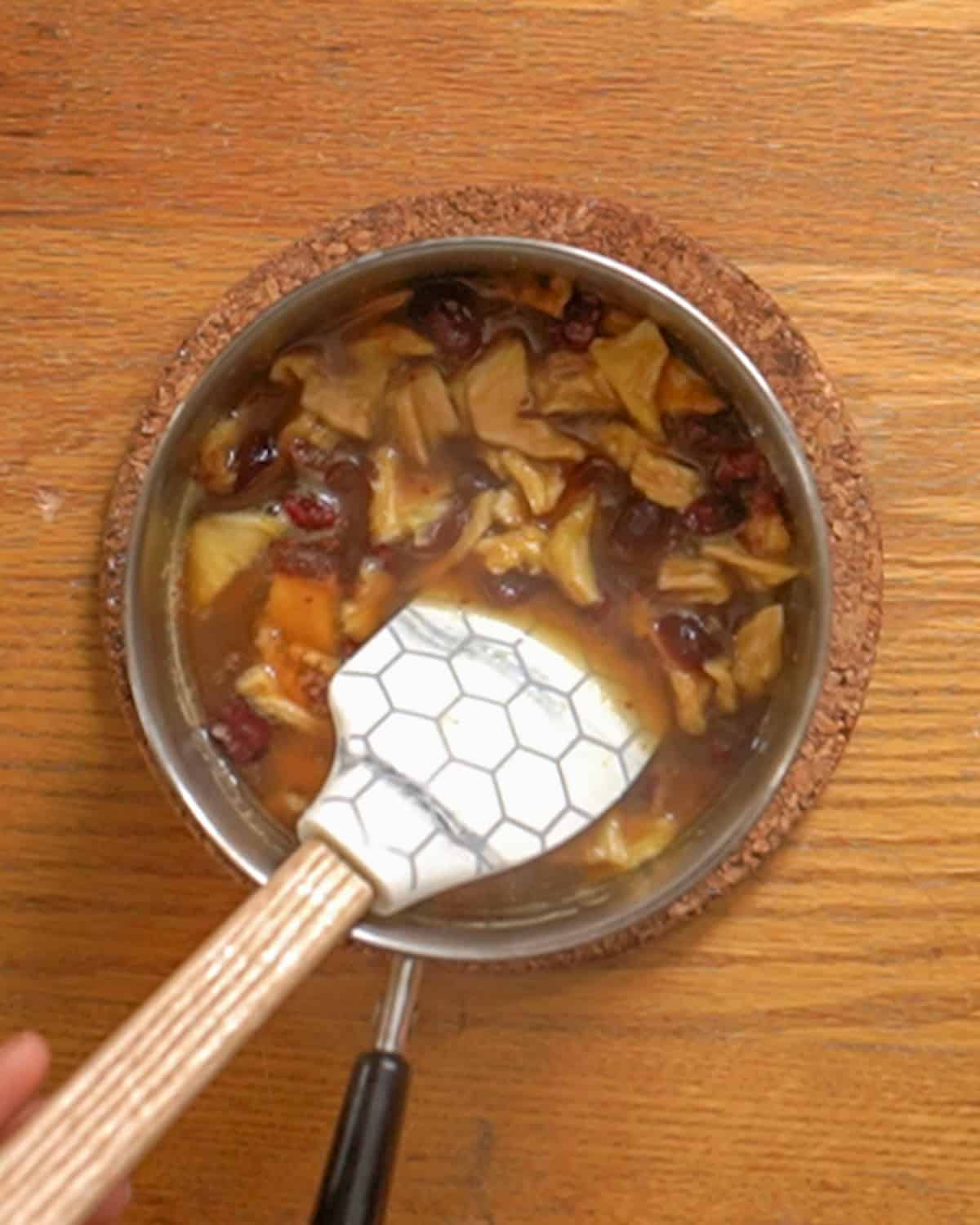 person stirring dried fruit cranberry sauce in a small saucepan with a spatula