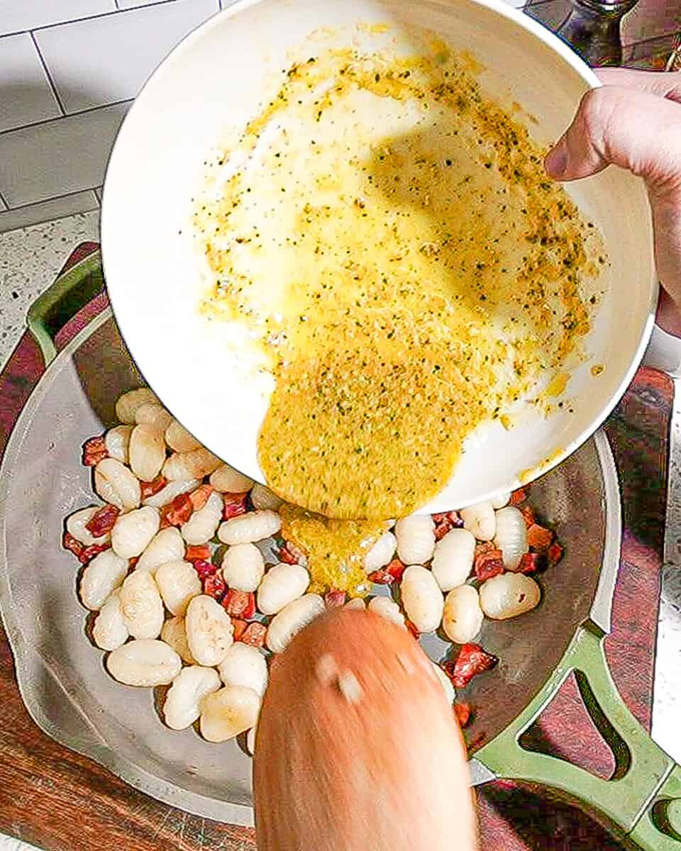 person pouring carbonara sauce onto pasta and pancetta