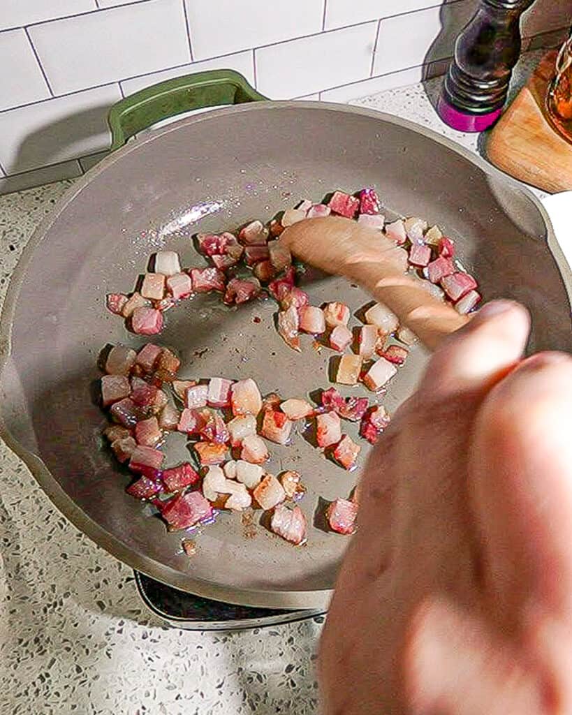 person stirring pancetta in green pan