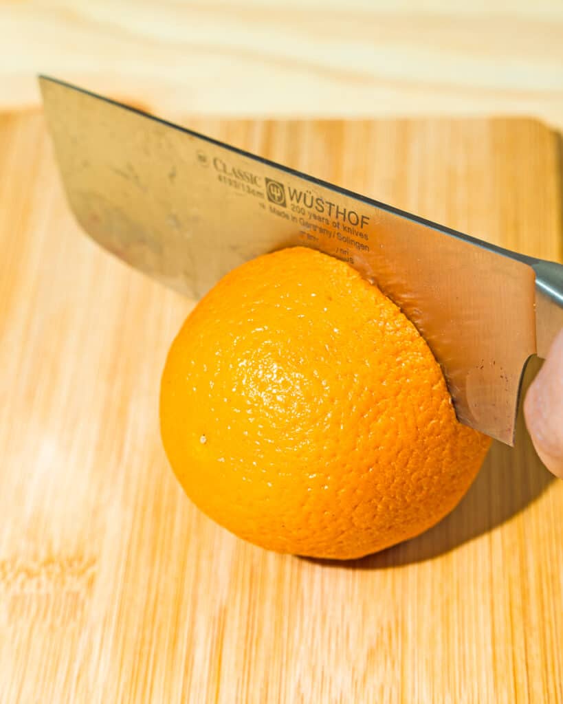 person cutting orange with knife on a wooden board