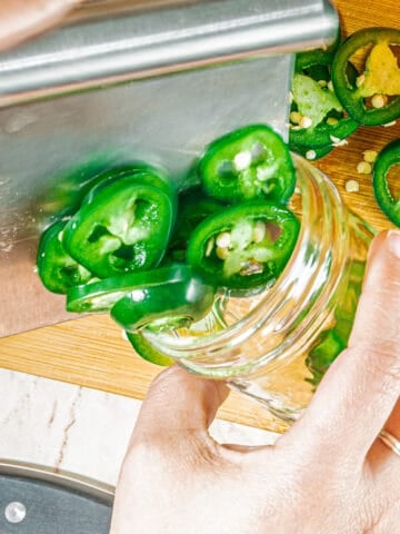 person adding peppers to a mason jar