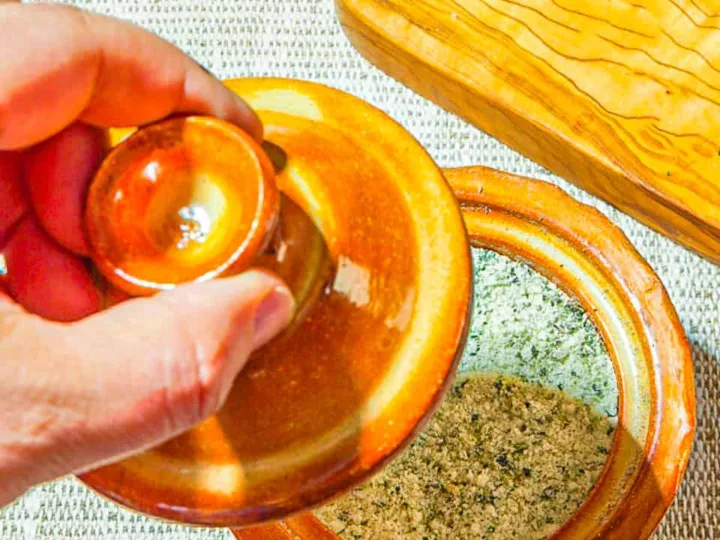person removing top on an orange ceramic salt keep of herb salt b