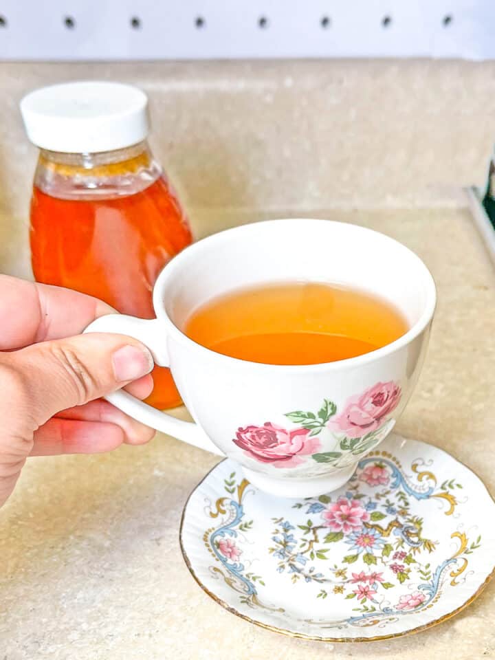person pickup up tea cup with lemon and honey tea. A bottle of honey in the background
