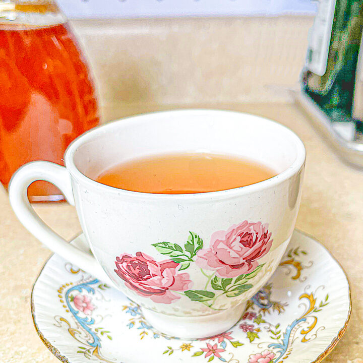 white tea cup with pink roses with lemon and honey tea. A bottle of honey in the background