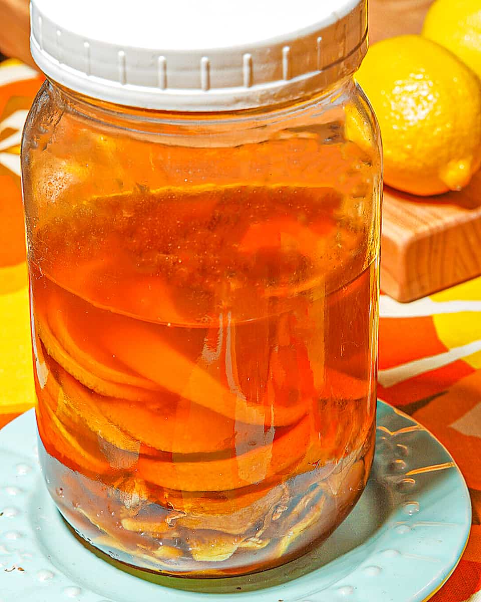 glass mason jar of lemons and ginger fermented in honey on a blue plate