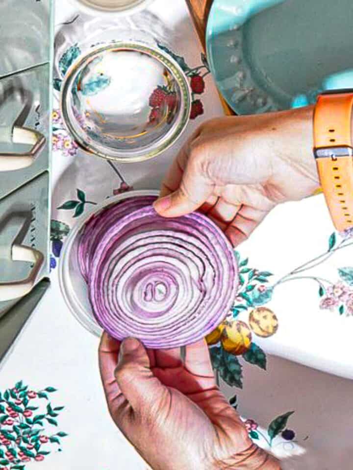 person adding red onion slices into a glass jar