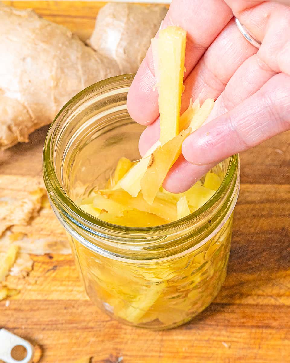 person adding slices of ginger to a small mason jar