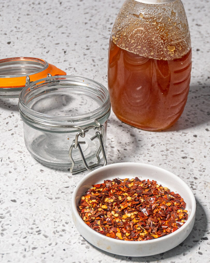 white dish with red pepper flakes, jar of honey and flip top mason jar