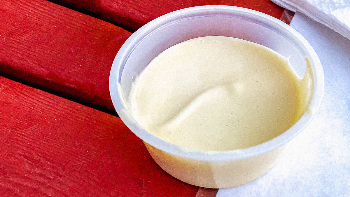 mayonaise in a plastic condiment cup on a red wooden picnic table