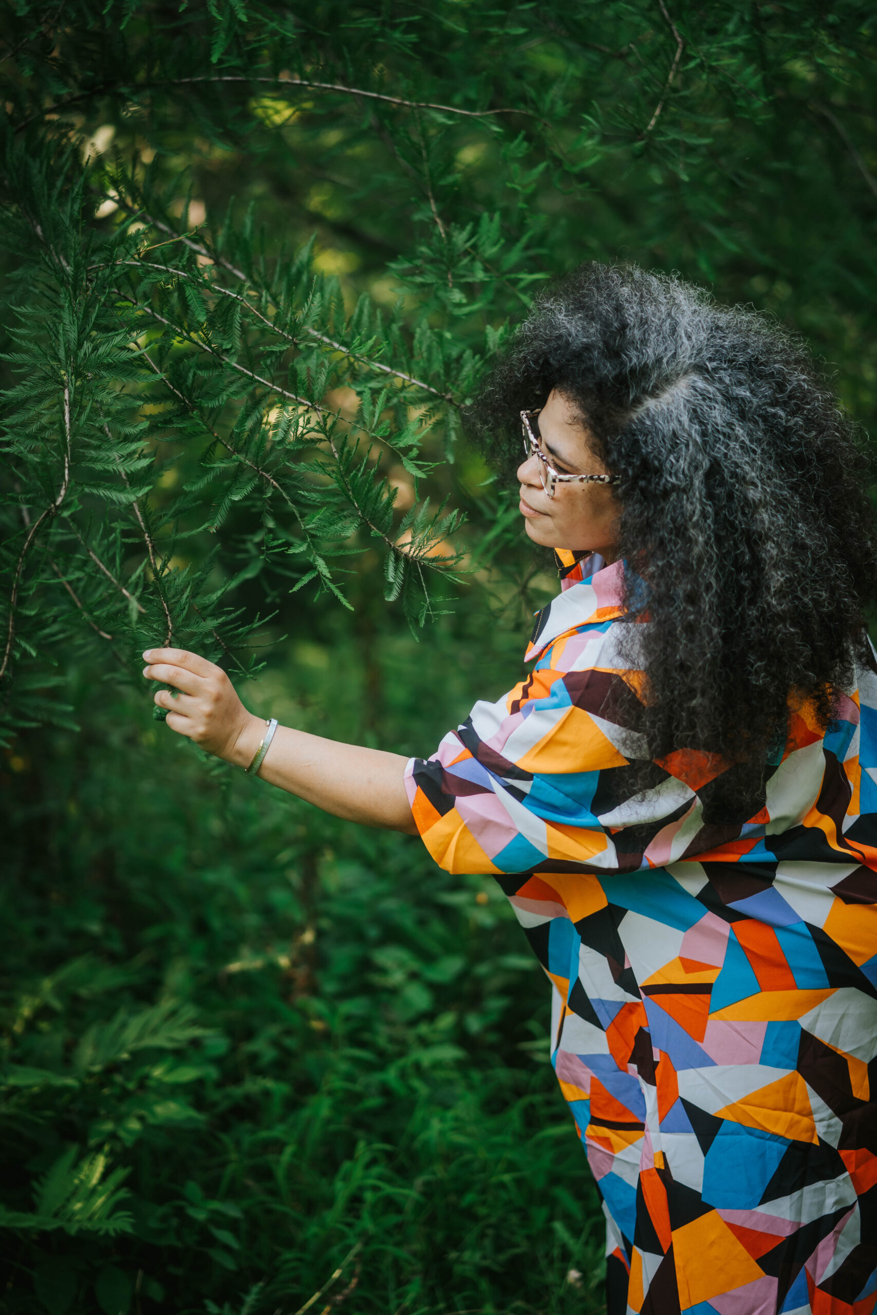 a person in a multi-colored dress reaching across in the picking something off of a tree