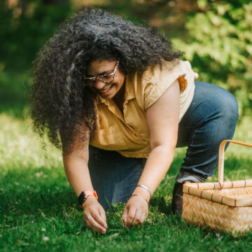 person in a pale yellow shirt with a picnic basket foraging in a green space