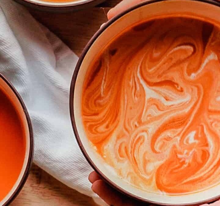 person holding butternut squash soup with two bowls of soup and loaf of bread