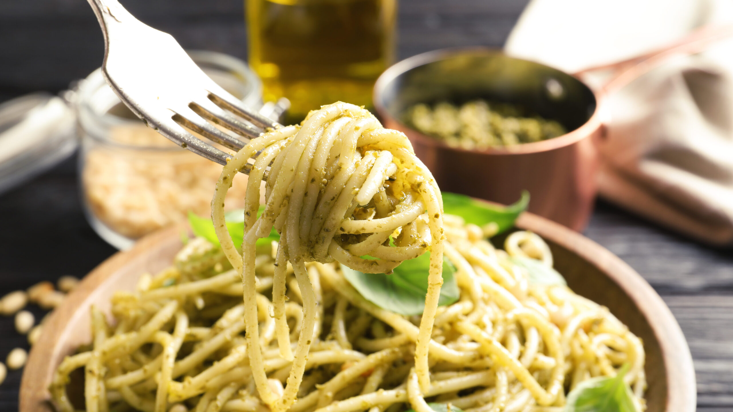 Fork with delicious basil pesto pasta over plate, closeup