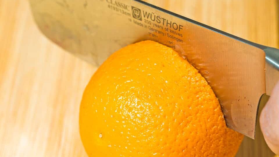 person cutting orange with knife on a wooden board