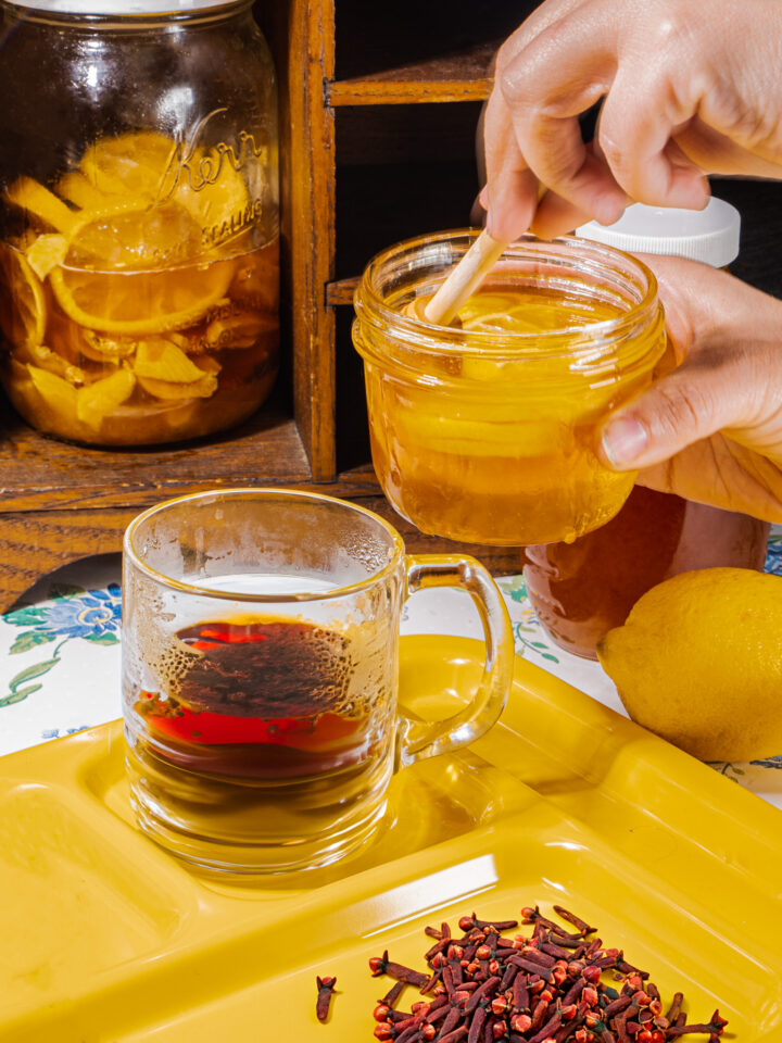 person adding lemon honey to a cup of clove tea