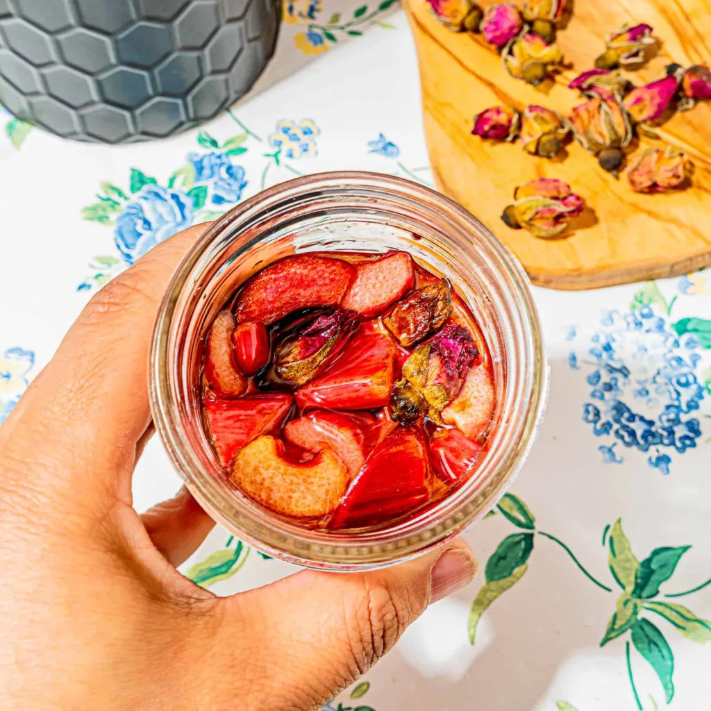 person holding 8 oz mason jar with picked rhubarb with rose buds in the far right corner