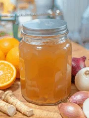 jar of fire cider with oranges, horseradishes and onions around it